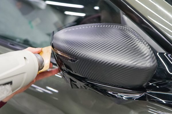 A car wrapping specialist applies a polyurethane film to the car. Selective focus. PPF protective film. The process of installing PPF on the side mirror. Car wrapping close-up.